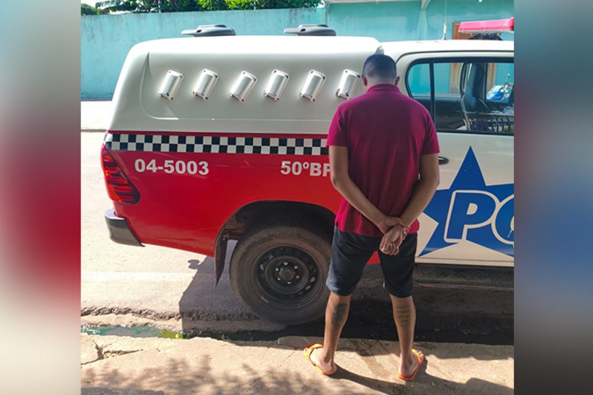 Homem de costas com mãos para trás ao lado de uma viatura policial.