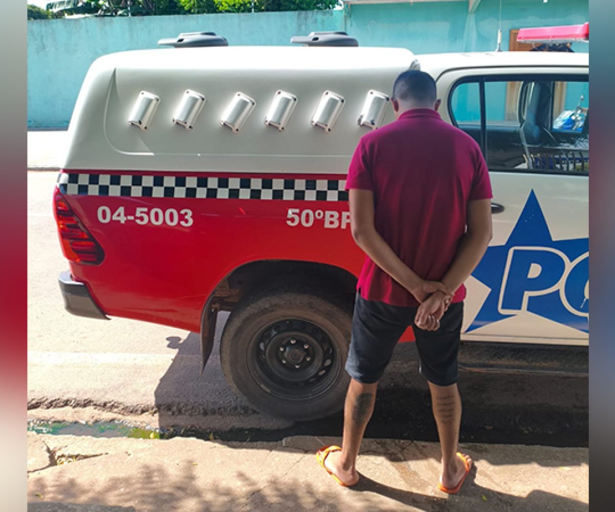 Homem de costas com mãos para trás ao lado de uma viatura policial.