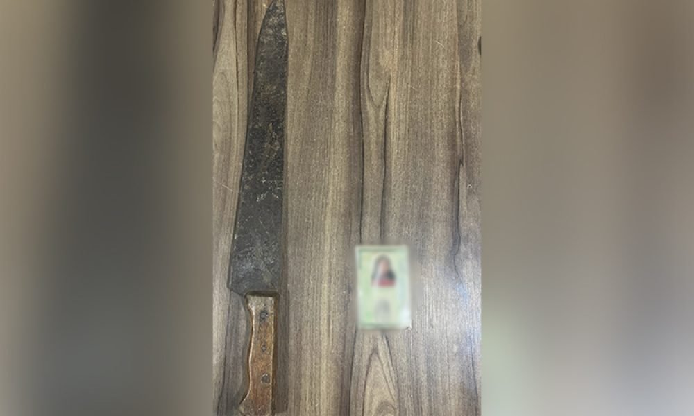 Faca grande e item borrado sobre superfície de madeira.