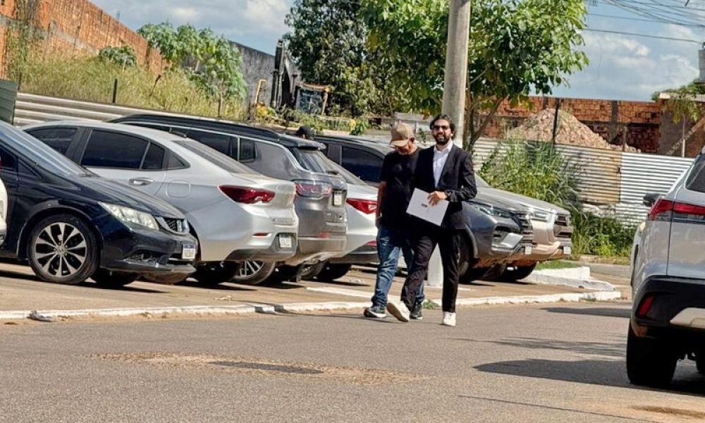 Dois homens caminhando na rua com carros estacionados ao fundo.