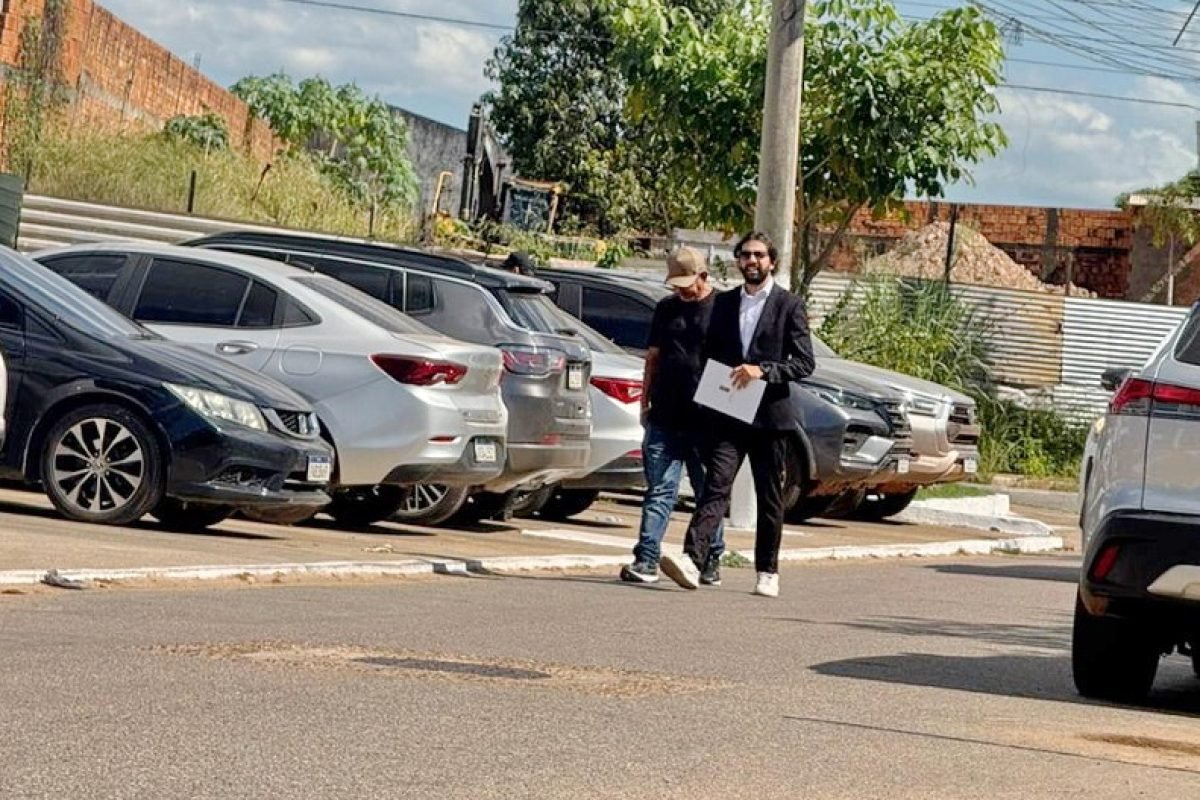 Dois homens caminhando na rua com carros estacionados ao fundo.