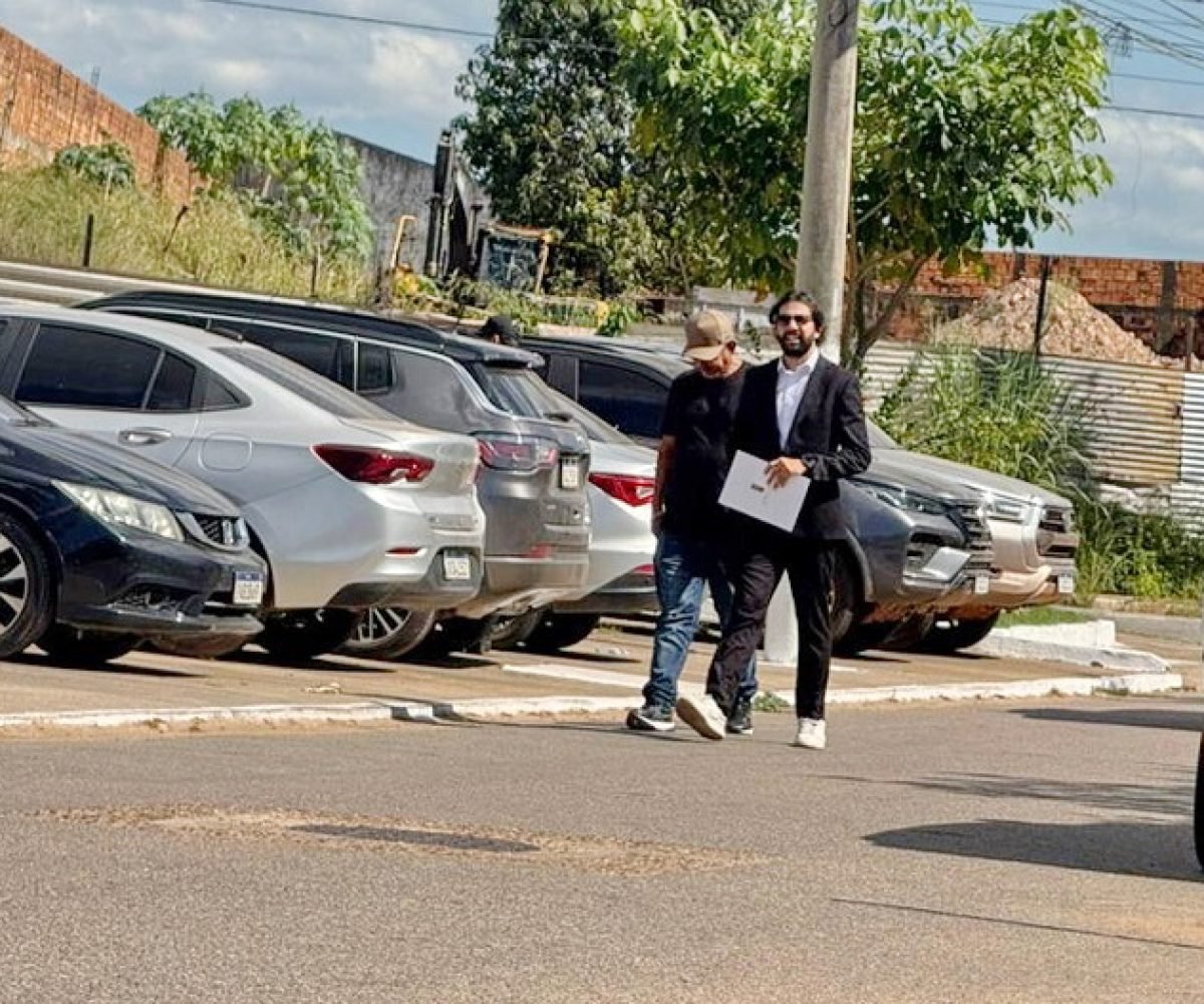 Dois homens caminhando na rua com carros estacionados ao fundo.