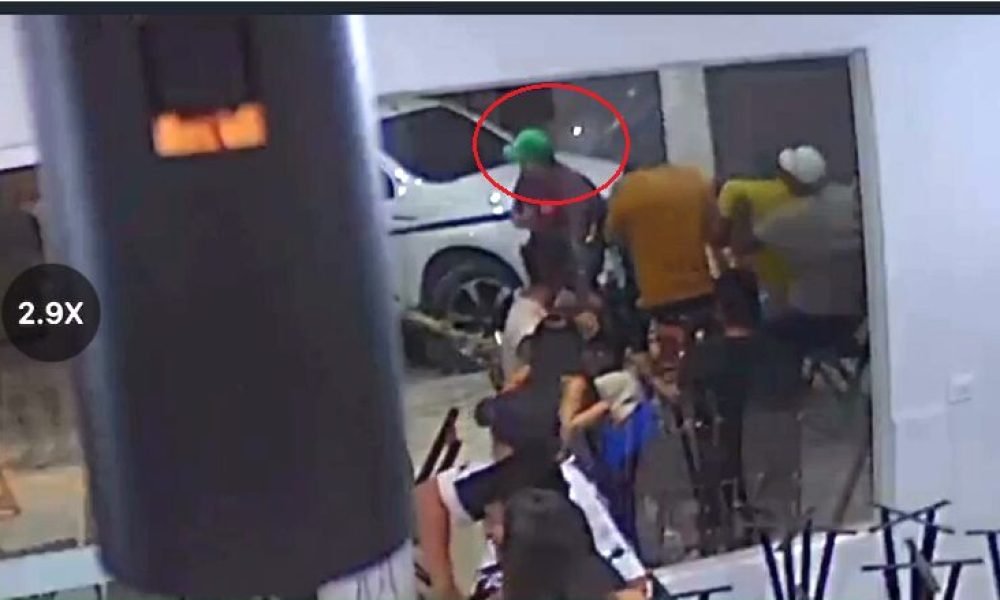 Grupo de pessoas em ambiente interno com carro branco ao fundo.