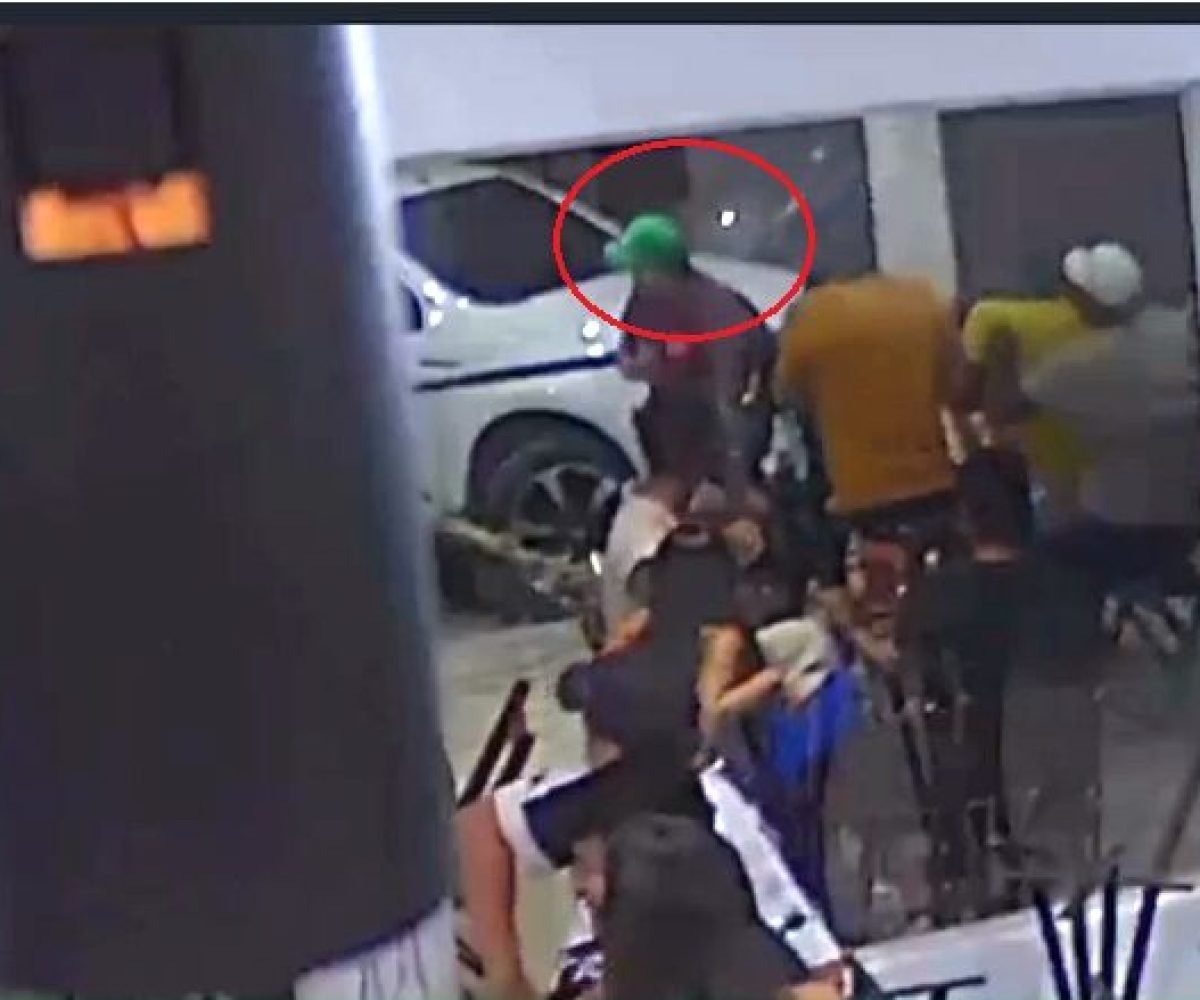 Grupo de pessoas em ambiente interno com carro branco ao fundo.