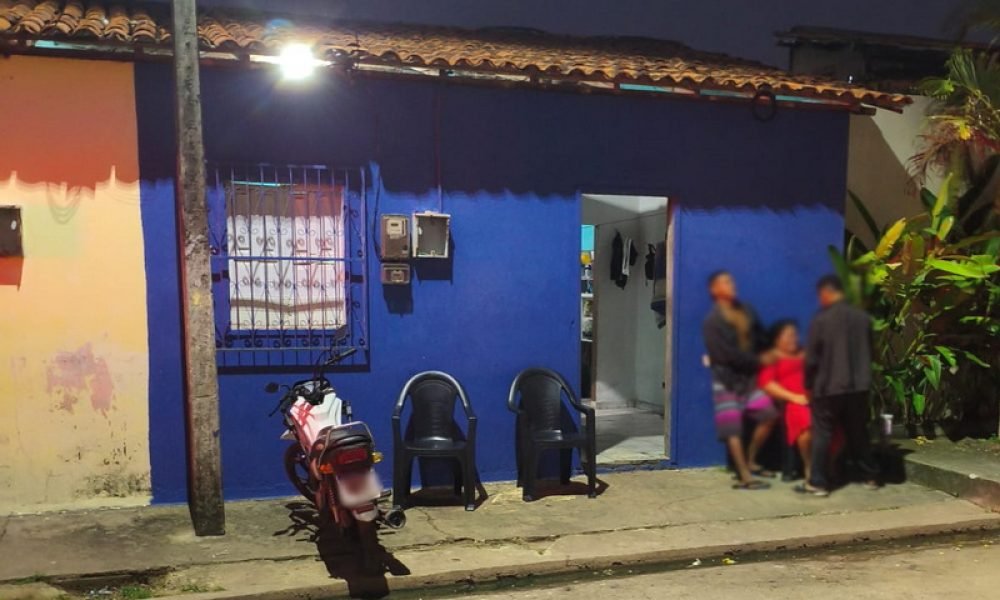 Casa azul vibrante com pessoas e motocicleta estacionada à noite.