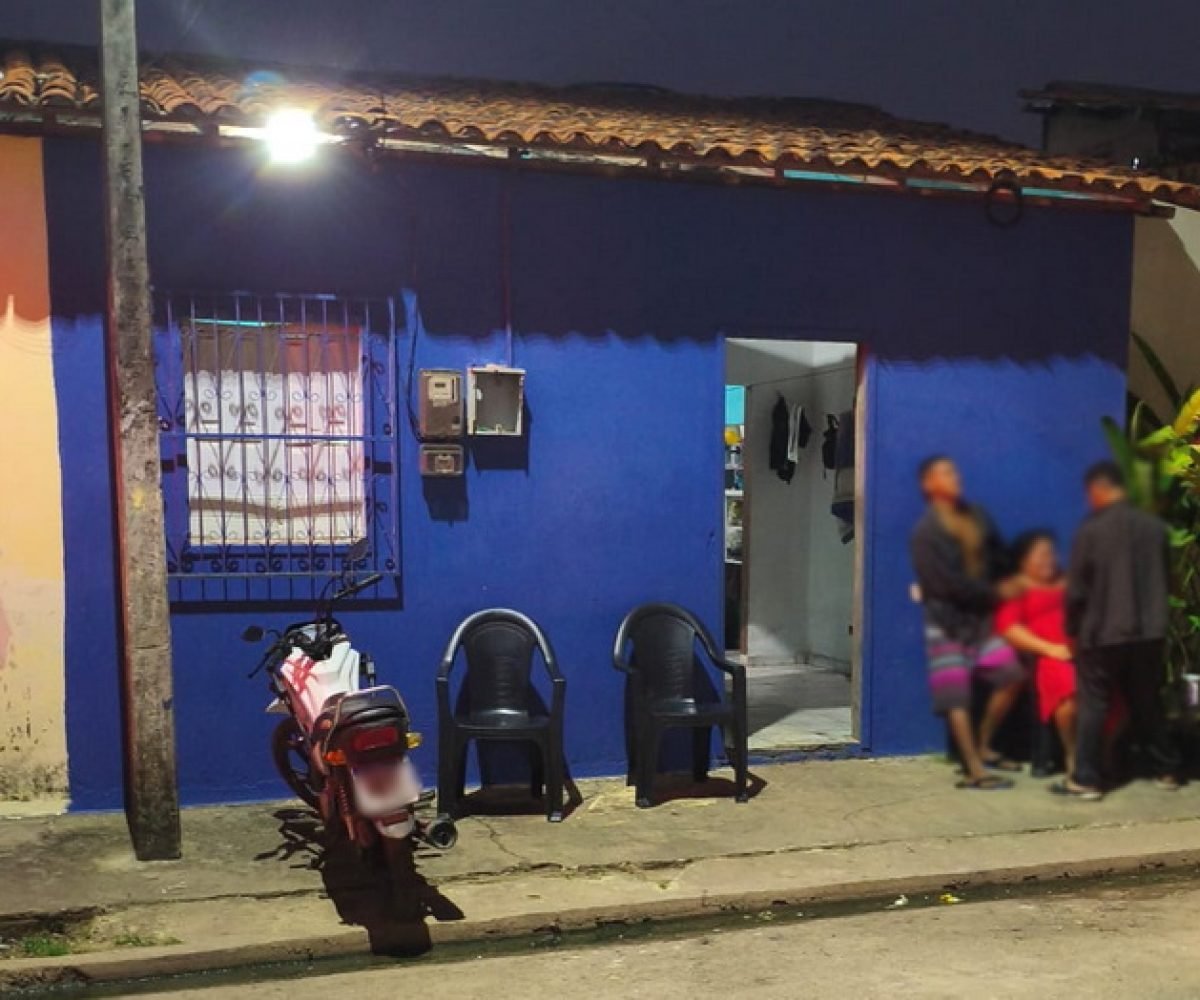 Casa azul vibrante com pessoas e motocicleta estacionada à noite.