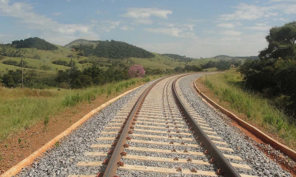 Trilhos de trem em curva atravessando uma paisagem rural montanhosa em dia ensolarado